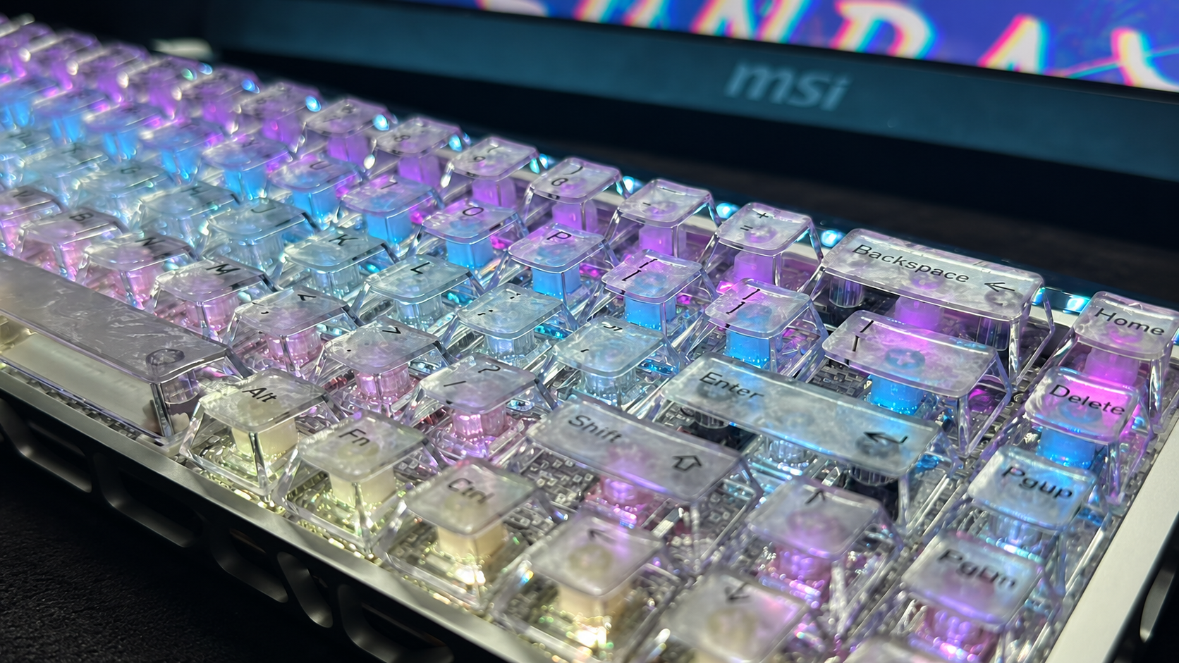 Translucent keyboard with colorful RGB lighting beside an MSI monitor